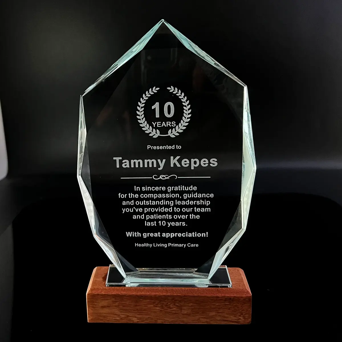 Personalized clear crystal-style years-of-service award on a wooden base